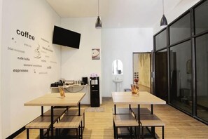 Un moderno caffè con tavoli e sedie, una macchina per il caffè e un televisore appeso al muro.
