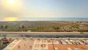 Une route côtière avec une portion goudronnée au premier plan, un ciel dégagé et une vue lointaine sur la mer.