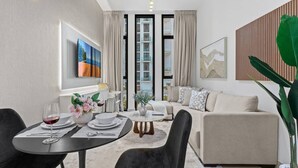 Un salon moderne avec un canapé, une table à manger et des chaises. On y trouve une grande fenêtre avec des rideaux, un tableau au mur et une plante.