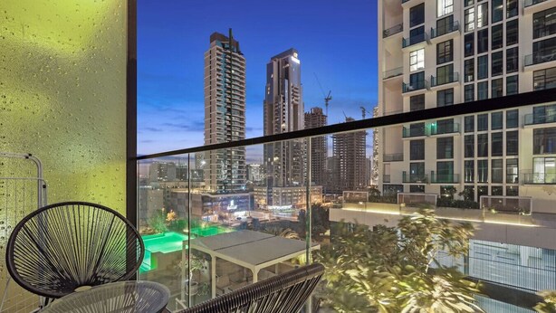 Un balcon offrant une vue sur le paysage urbain au crépuscule, avec des immeubles modernes et des piscines.