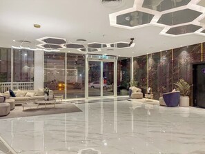 A modern lobby with a glass entrance, a seating area with sofas and a coffee table, and a decorative ceiling.