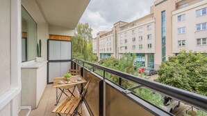 A balcony with a table and chairs, a potted plant, and a view of surrounding buildings and greenery. - Spacious Apartment | Air Conditioning, Balcony, close to the Stadium (Warszawa)