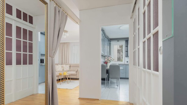 A hallway with a mirror, a beige sofa, a small table with a yellow object, and a kitchen area in the background. - Spacious Apartment | Air Conditioning, Balcony, close to the Stadium (Warszawa)