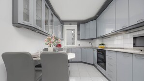 A modern kitchen with grey cabinets, a dining area with two chairs, and a small table with a vase of flowers. - Spacious Apartment | Air Conditioning, Balcony, close to the Stadium (Warszawa)