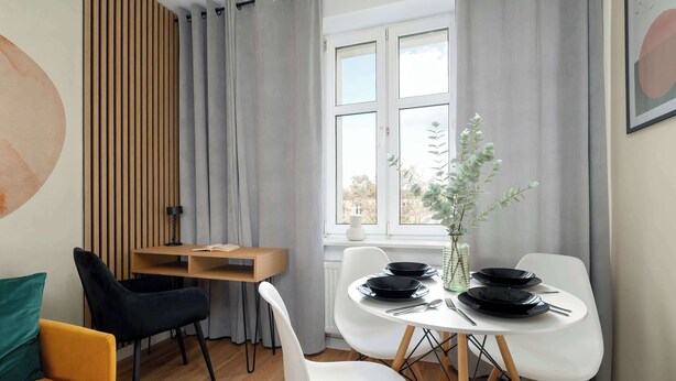 Ein Essbereich mit einem Tisch für vier Personen, einem Holztisch und einem Fenster mit Vorhängen.