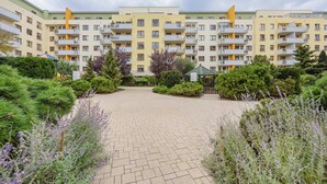 Un edificio residencial de varios pisos con balcones, rodeado de jardines cuidados y un patio empedrado.