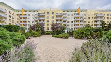 A multi-story residential building with balconies, surrounded by well-maintained gardens and a paved courtyard.