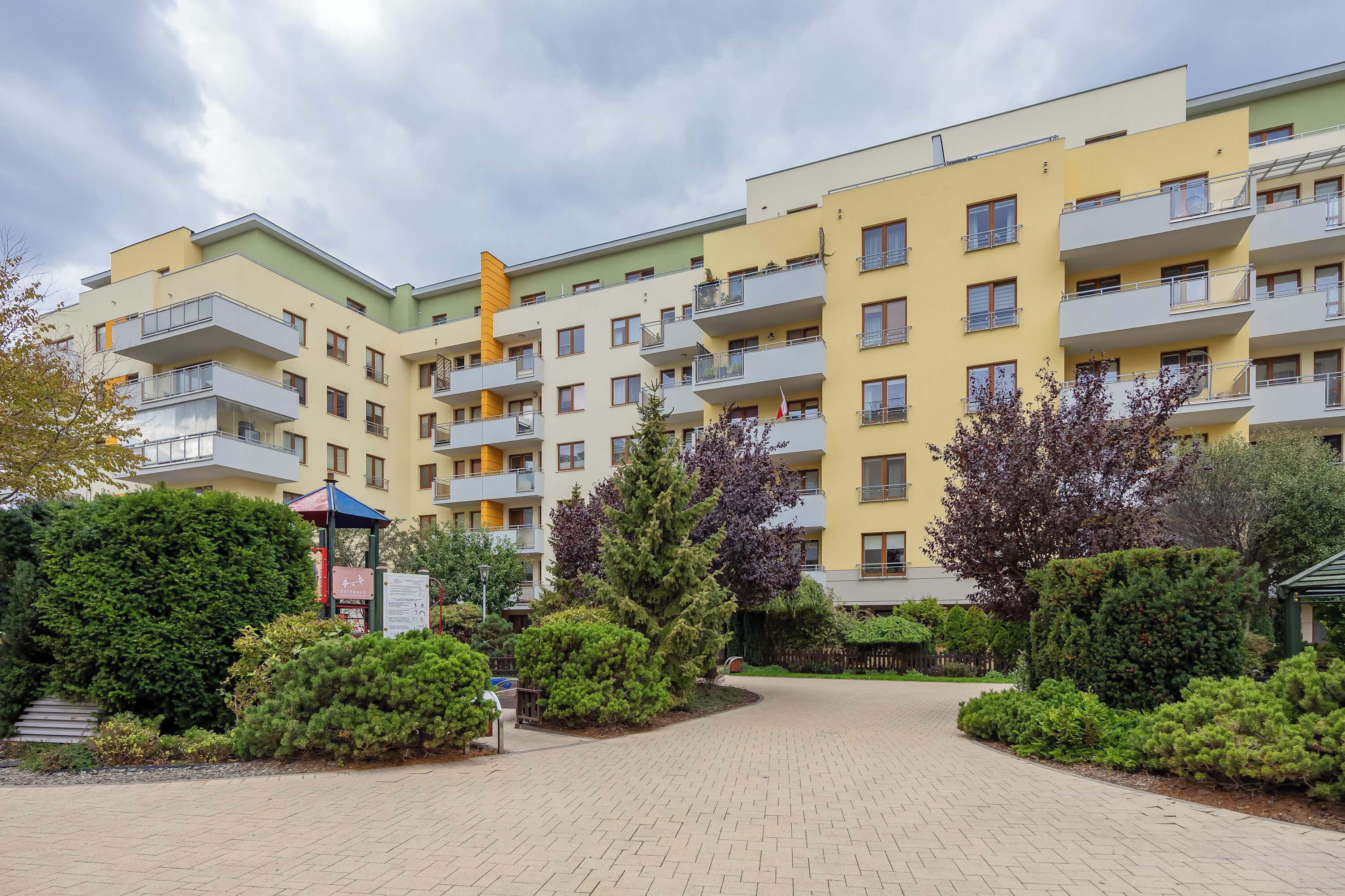 Un edificio residencial de varios pisos con balcones, un patio empedrado y abundante vegetación.