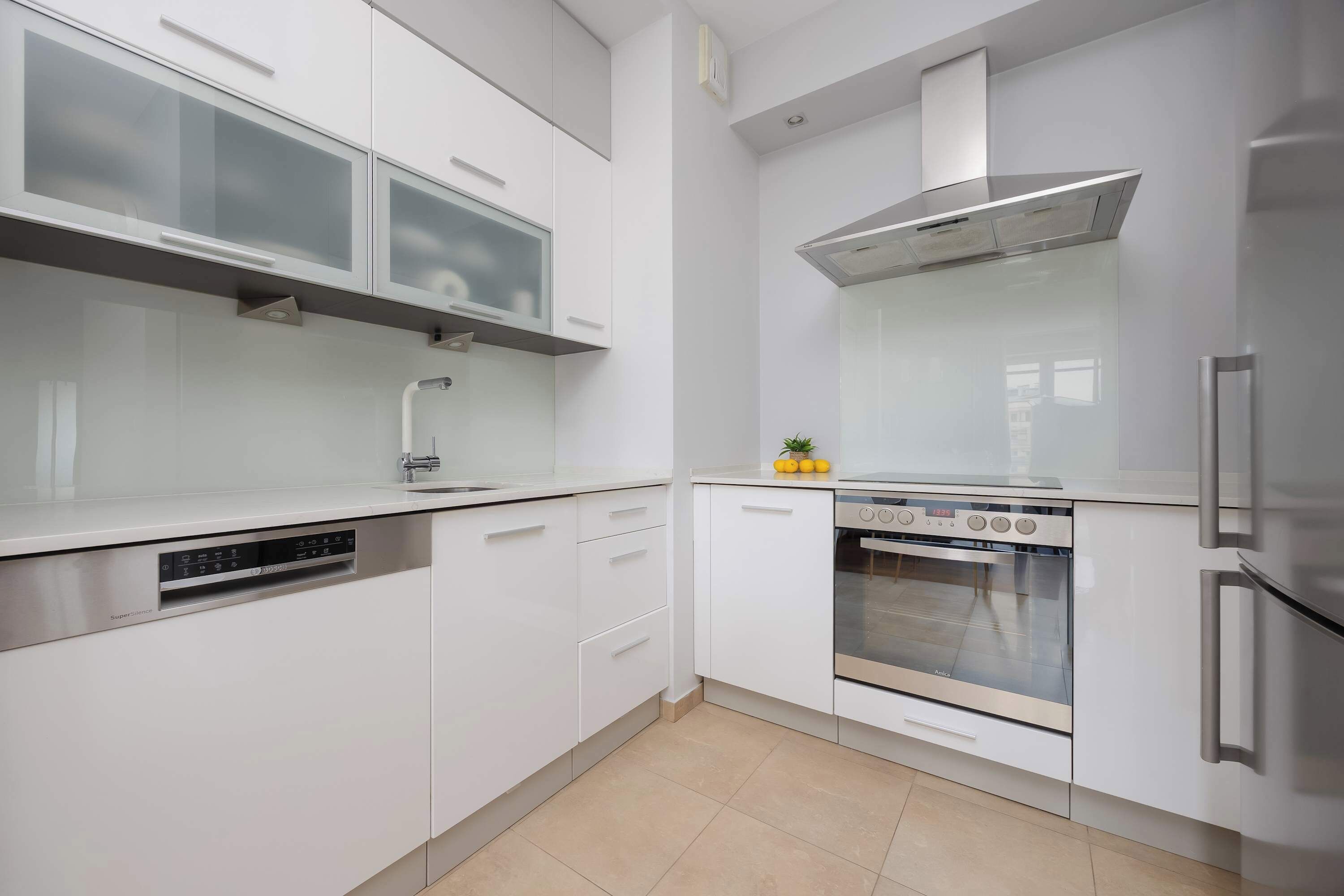 A modern kitchen with white cabinetry, a stainless steel dishwasher, an oven, and a refrigerator.
