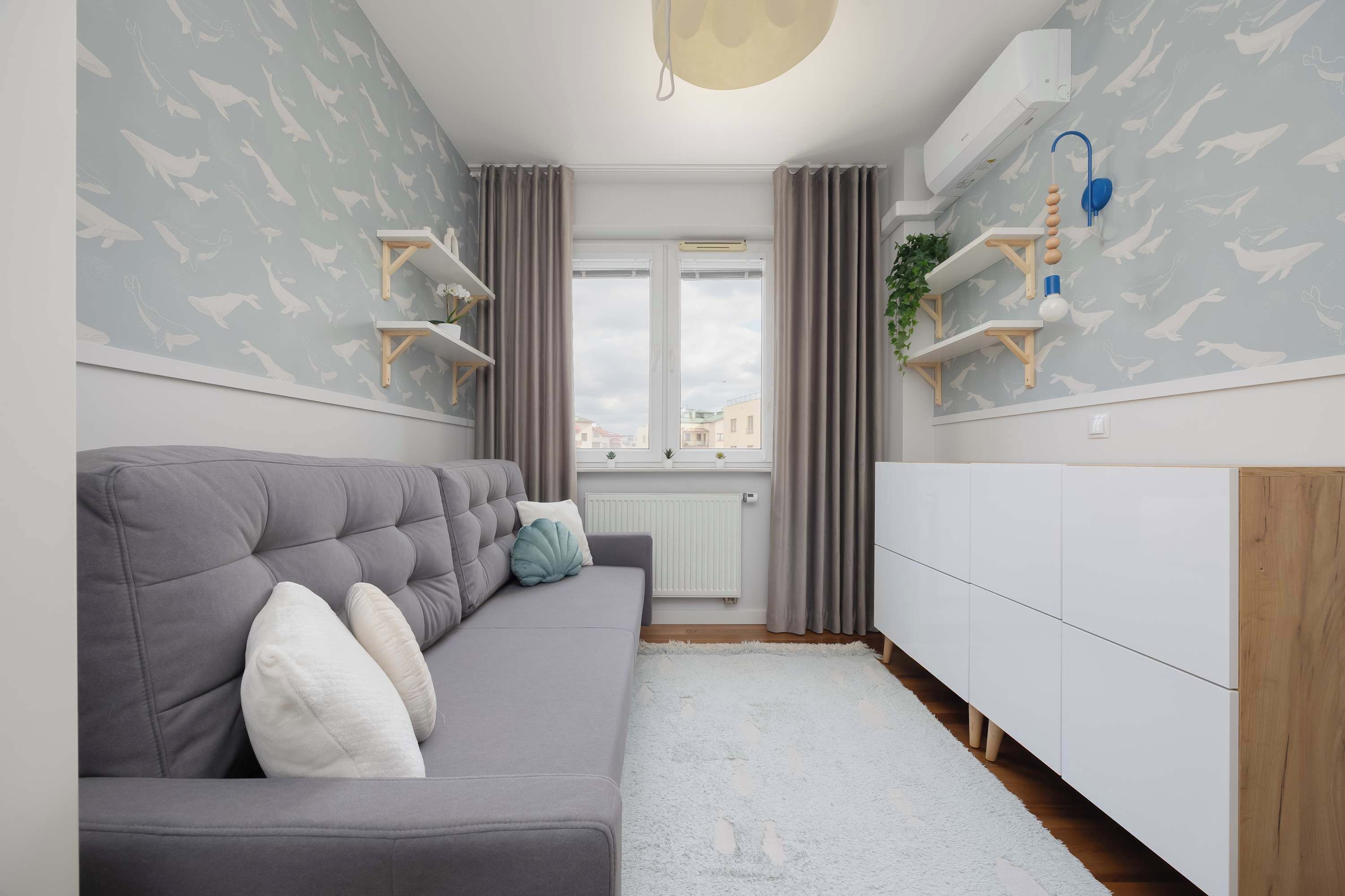 Un salon moderne avec un canapé gris, un meuble de rangement blanc et une fenêtre avec des rideaux.