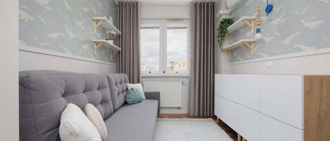 Un salon moderne avec un canapé gris, un meuble de rangement blanc et une fenêtre avec des rideaux.