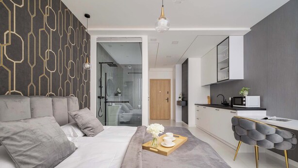Une chambre à coucher moderne avec un grand lit, une table de chevet avec un plateau, et une vue sur la cuisine.