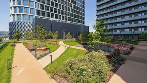 Un bâtiment moderne à la façade incurvée, doté d’un jardin bien entretenu avec des allées et des espaces pour s’asseoir.