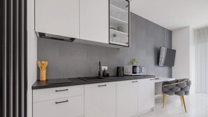 Une cuisine moderne avec des meubles blancs, un plan de travail noir et une chaise rembourrée de couleur grise aux pieds dorés.