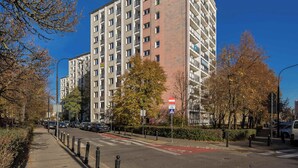 Un edificio residencial de varios pisos con balcones, un carril bici rojo y un cielo azul despejado.