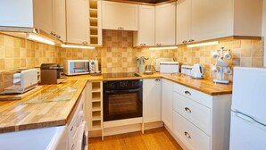 A compact kitchen with white cabinets, a built-in oven, a microwave, and a toaster. - Host & Stay | Dairy Cottages (Masham)