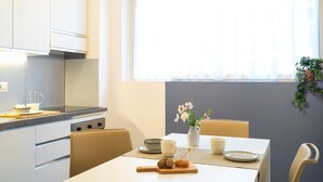 A modern kitchen with a dining table set for two, featuring a vase of flowers, a cutting board with nuts, and a bowl of fruit. - 7Studios - 7 Blue (Milano)