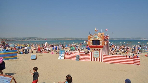 A beach with a striped tent and a lifeguard tower. - Harbourside Apartment (Weymouth)