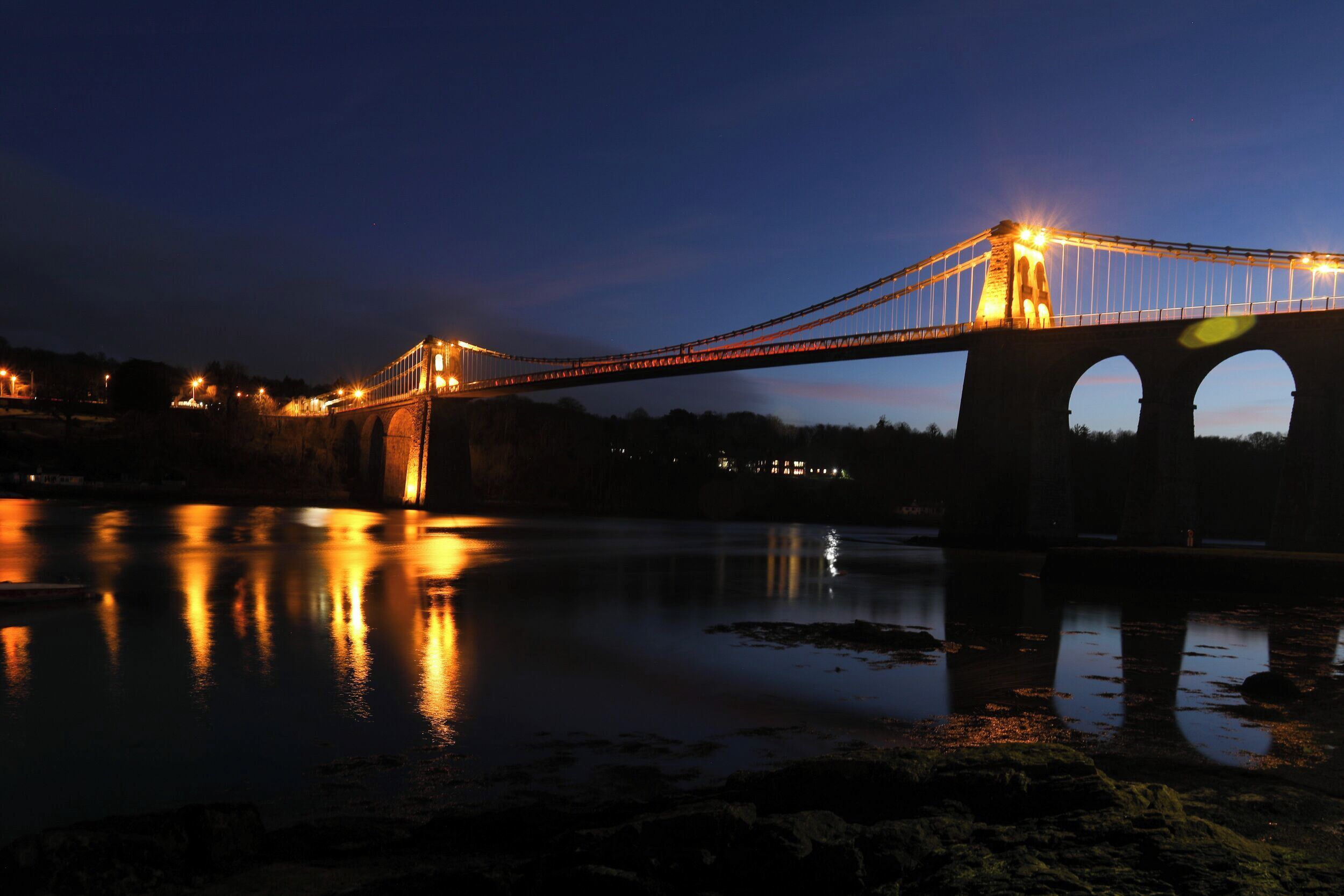 A bridge at night with lights reflecting on the water.