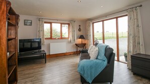 A living room with a television, a sofa, a lamp, and a window with curtains. - Bluebell Cottage (Tenbury Wells)