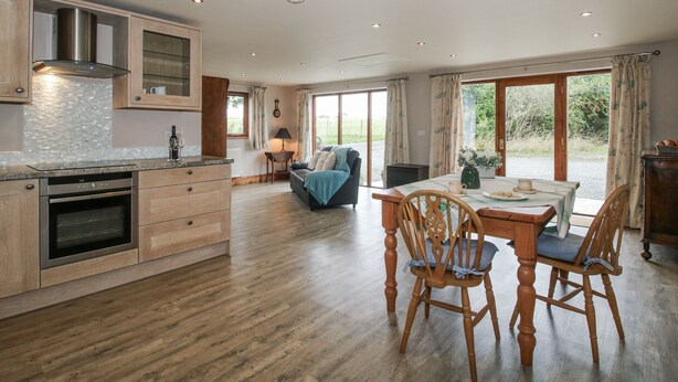 A spacious kitchen with wooden cabinets, a built-in oven, and a large dining area with a table and chairs. - Bluebell Cottage (Tenbury Wells)