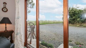 A room with a wooden-framed sliding glass door leading to a gravel path and a metal windmill. - Bluebell Cottage (Tenbury Wells)