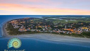 Eine Luftaufnahme von Beachside Colony, einer Küstengemeinde mit einer Mischung aus Wohn- und Geschäftshäusern, umgeben von Wasser und Grünflächen.