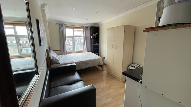 A bedroom with a bed, a wardrobe, a desk, and a window with curtains. - Cozy Studio in Stoke Newington (London)