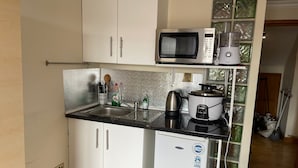 A compact kitchen with white cabinets, a stainless steel sink, a microwave, a slow cooker, and a small refrigerator. - Cozy Studio in Stoke Newington (London)