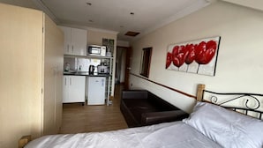 A bedroom with a bed, a small kitchenette, and a red flower painting on the wall. - Cozy Studio in Stoke Newington (London)