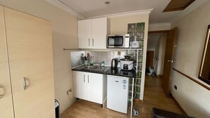 A compact kitchen with white cabinets, a microwave, a coffee maker, and a kettle. - Cozy Studio in Stoke Newington (London)