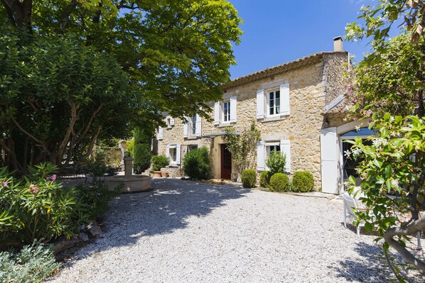 A stone building with a gravel driveway, surrounded by greenery and a clear blue sky. - Gite Grand Luberon chez Manon en Luberon (Lagnes)