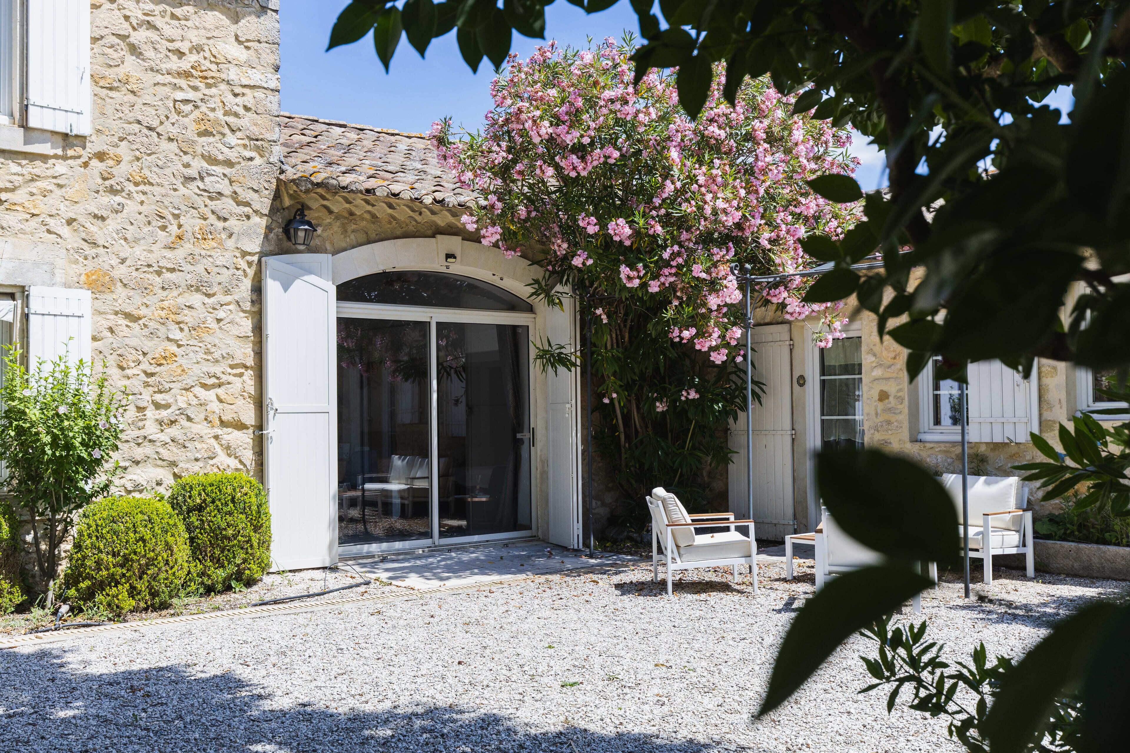 A stone building with a gravel courtyard, white chairs, and a blooming pink tree.