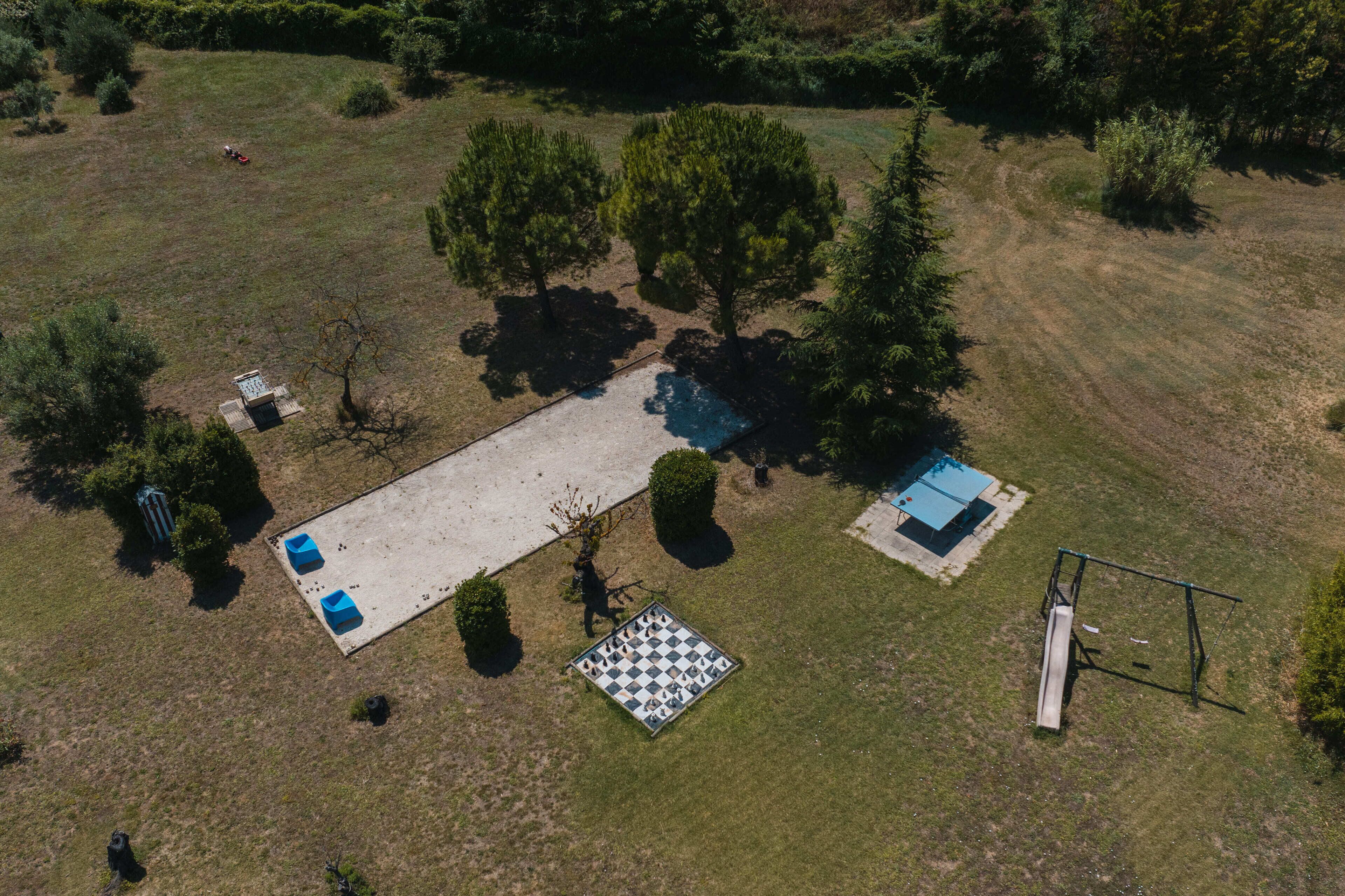 An aerial view of a property with a large open lawn, a swimming pool, a tennis court, and a small building.