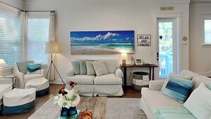 Een woonkamer met een schilderij met een strandthema, een bordje met de tekst "REACH HOUSE" en een bordje met de tekst "RELAX AND UNWIND".