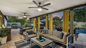 Un patio extérieur abrité, aménagé avec un canapé, des fauteuils, une table et un ventilateur de plafond.