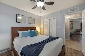 A bedroom with a bed, a ceiling fan, and two framed pictures on the wall.