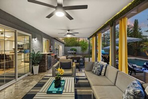 A modern outdoor living area with a ceiling fan, a barbecue grill, and a poolside seating area.