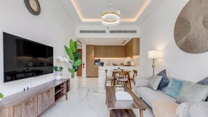 A modern living room with a flat-screen TV, wooden furniture, a dining area, and a kitchen in the background. - GLOBALSTAY Azizi Riviera 59 (Dubai)