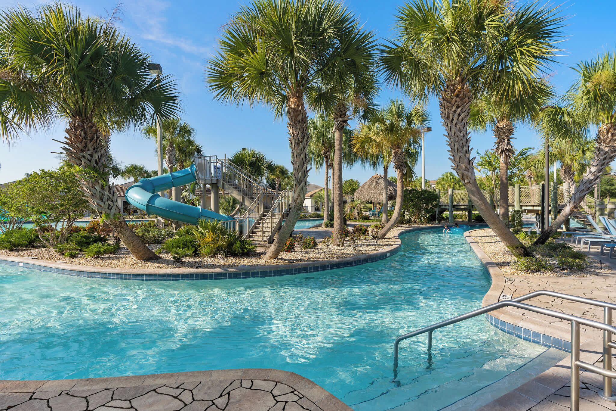 A swimming pool with a water slide, palm trees, and a thatched-roof structure.
