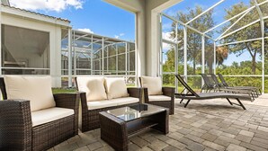 Een overdekt terras met rieten meubels, een glazen tafel en uitzicht op de omliggende groene omgeving.