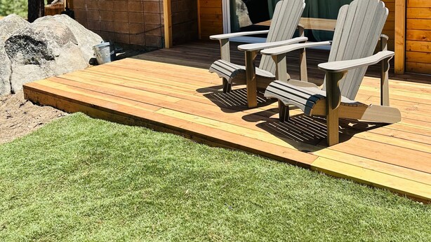 A wooden deck with Adirondack chairs, a brick chimney, and a glass door leading to a covered area. - Nvh0650 - Woodland Escape 2 Bedroom Home (Stateline)