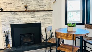 A room with a fireplace, stone wall, wooden floor, and a round table with chairs. - Nvh0650 - Woodland Escape 2 Bedroom Home (Stateline)