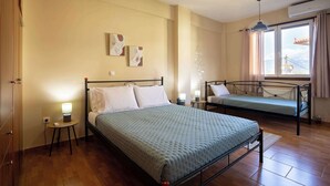 Quarto de hotel com duas camas de solteiro, uma pequena mesa de cabeceira com abajur, uma obra de arte na parede e uma janela com cortinas.