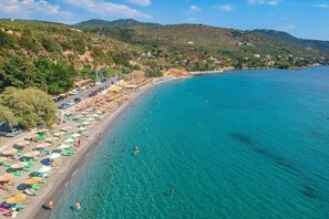 Una playa costera con aguas turquesas cristalinas, una fila de sombrillas y una carretera paralela a la orilla.
