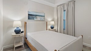 A hotel room with a bed, two bedside tables with lamps, a painting on the wall, and a window with curtains. - Terrace At Pelican Beach 0107 3 Bedroom Condo (Destin)