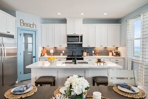 A modern kitchen with white cabinets, a central island, and a microwave. - Oceanfront Manor 4 Bedroom Home (Port Bolivar)