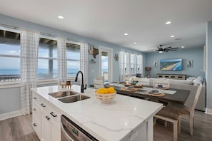 A modern kitchen with a large island, a dining area, and a view of the ocean. - Oceanfront Manor 4 Bedroom Home (Port Bolivar)