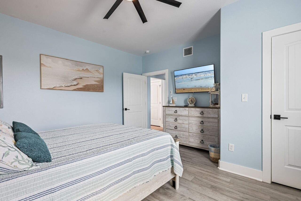Un dormitorio con cama, cómoda, televisor y un cuadro en la pared.