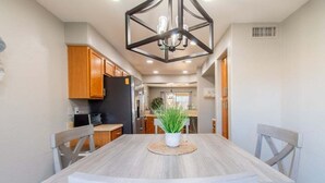 A dining area with a wooden table and chairs, a chandelier, and a potted plant. - Casa Aria 4br Home & Heated Pool 4 Bedroom Home (Casa Grande)